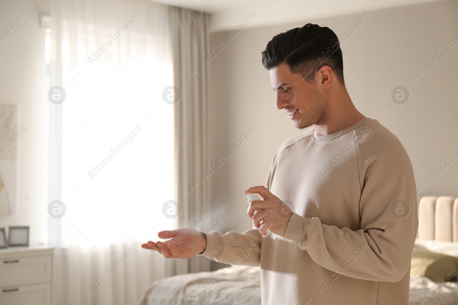 Photo of Man applying spray sanitizer onto hand at home