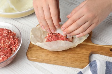 Photo of Woman preparing stuffed cabbage rolls at white wooden table, closeup