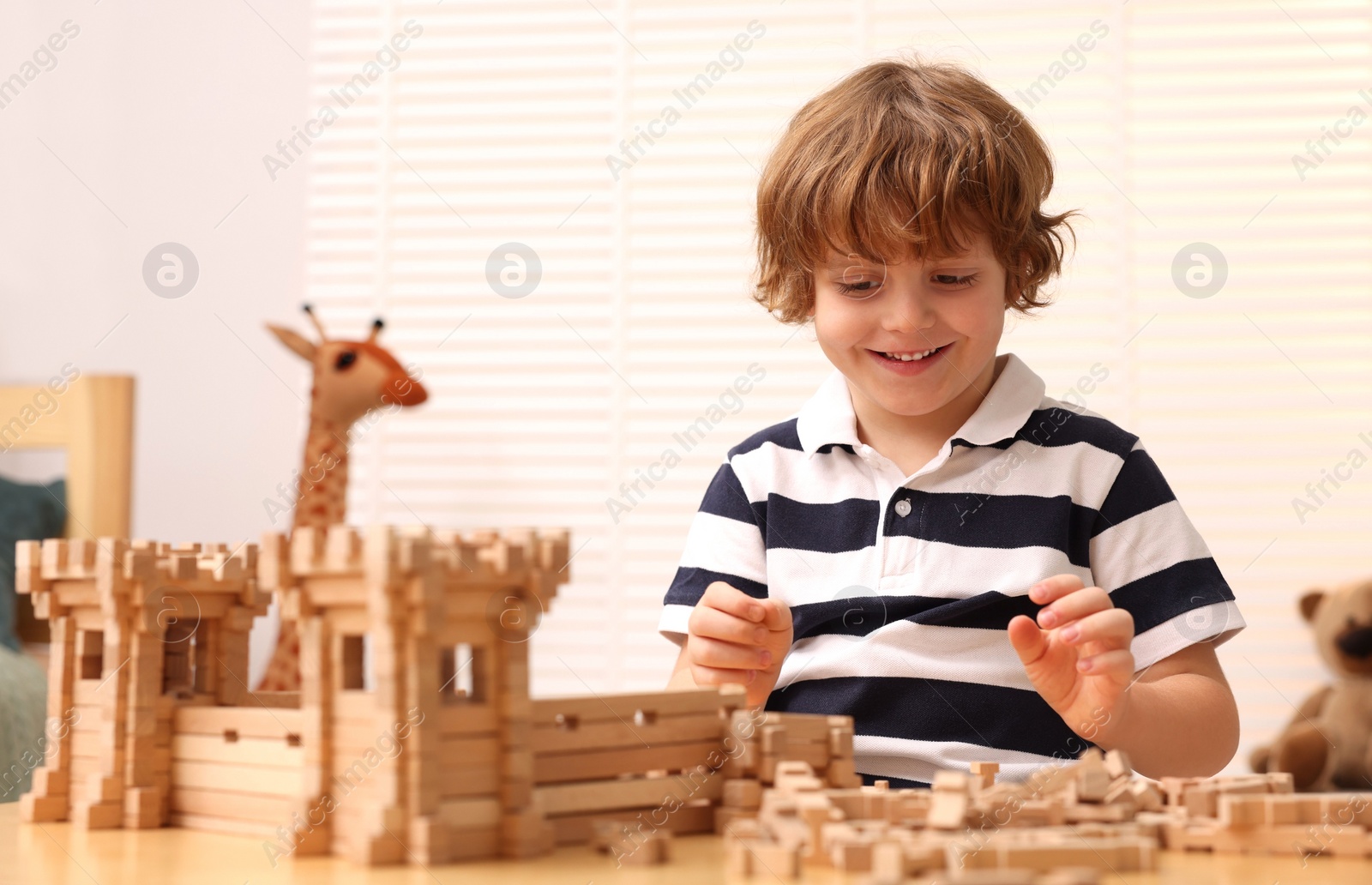 Photo of Little boy playing with wooden entry gate at table in room. Child's toy