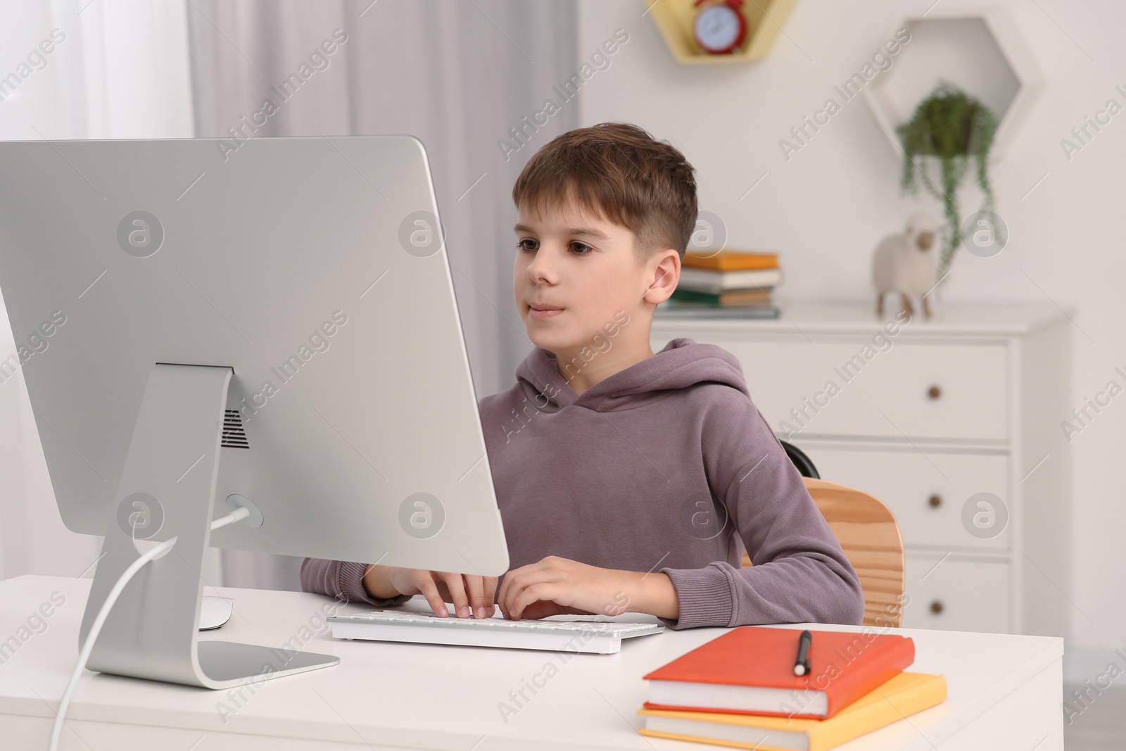 Photo of Boy using computer at desk in room. Home workplace