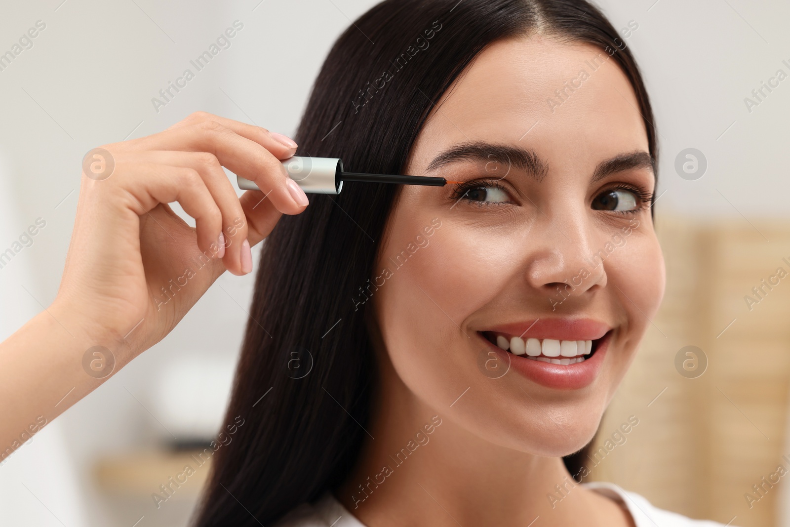 Photo of Beautiful woman applying serum onto her eyelashes indoors, closeup. Cosmetic product