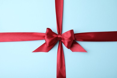 Red satin ribbon with bow on light blue background, top view