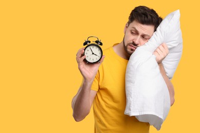 Photo of Tired man with alarm clock and pillow on yellow background, space for text. Insomnia problem