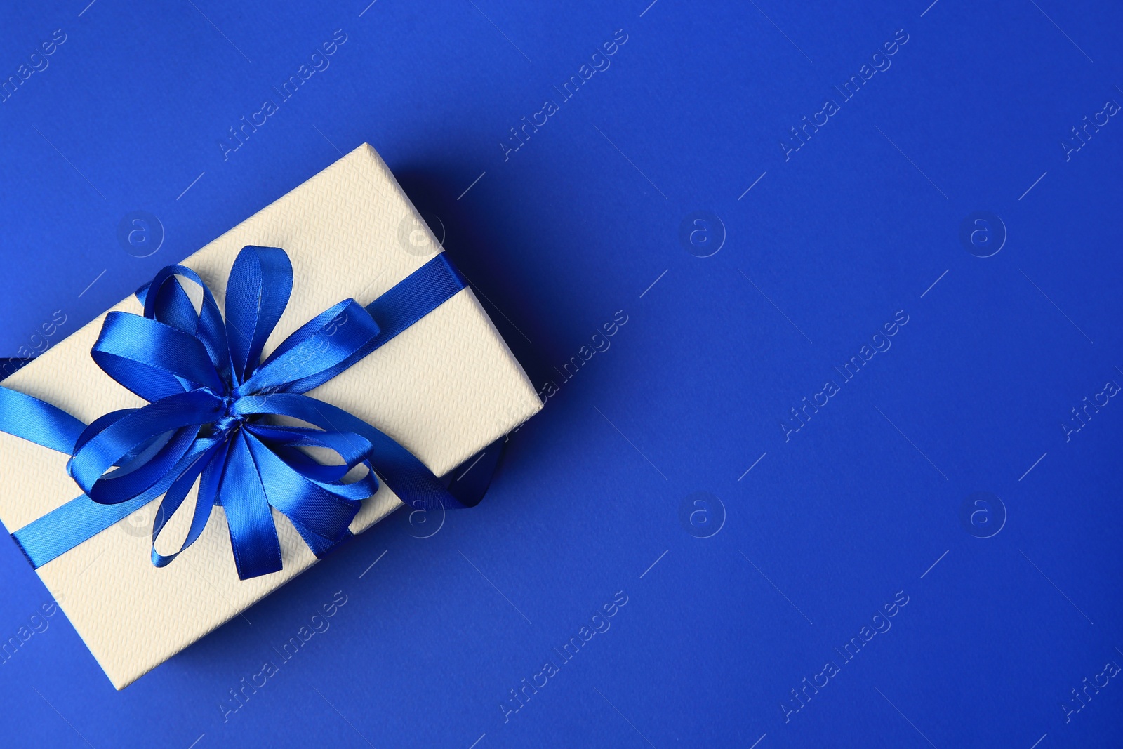 Photo of Beautiful gift box with bow on blue background, top view. Space for text