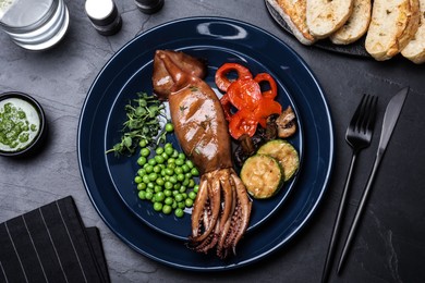 Photo of Delicious grilled squid served on black table, flat lay