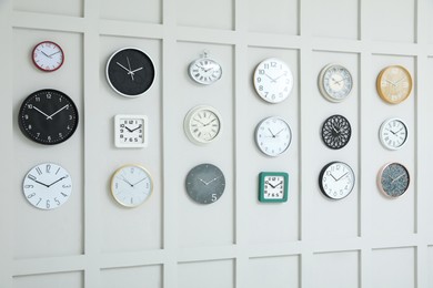 Many different clocks hanging on white wall.