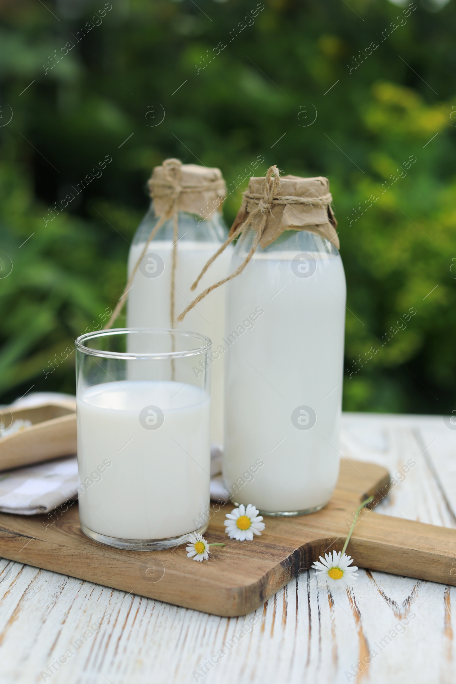 Photo of Tasty fresh milk and chamomile flowers on white wooden table outdoors