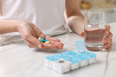 Woman with pills, organizer and glass of water at white marble table, closeup