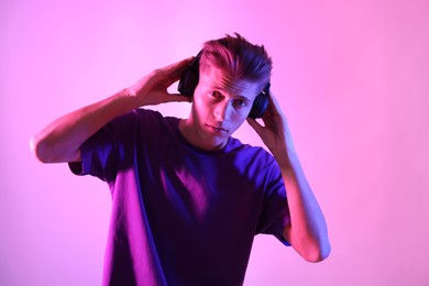 Photo of Young man with headphones on pink background in neon lights