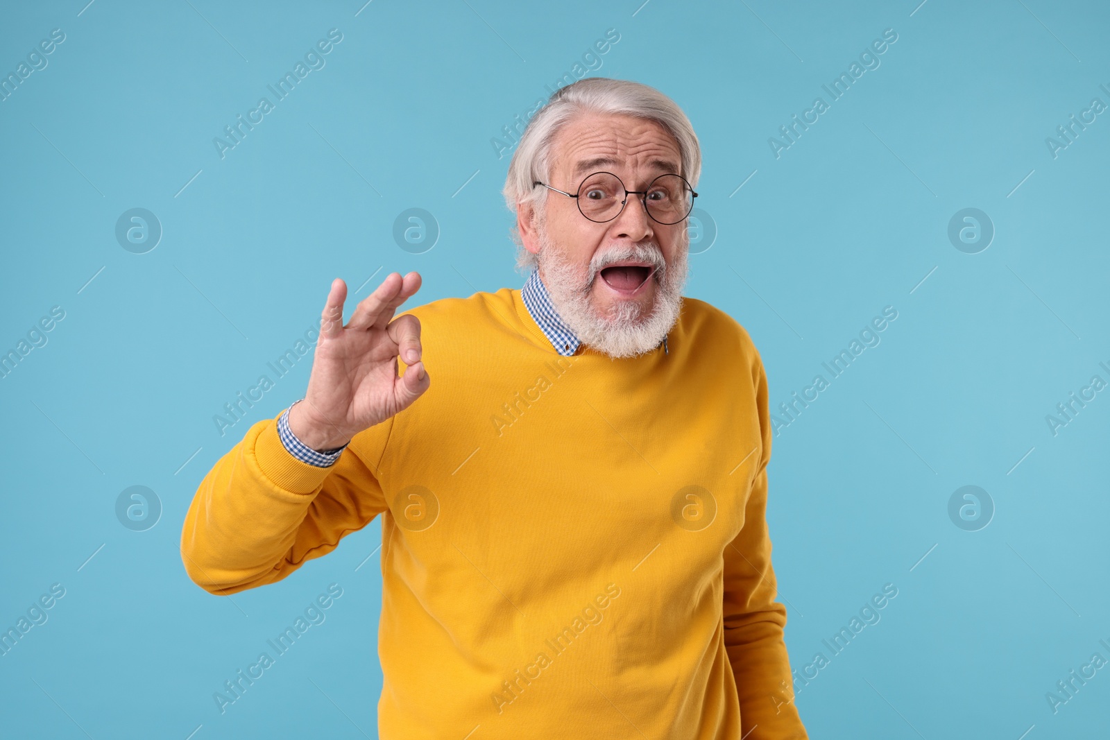 Photo of Portrait of stylish grandpa with glasses showing ok gesture on light blue background