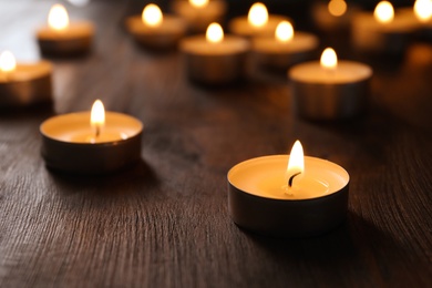 Photo of Wax candles burning on table in darkness, closeup