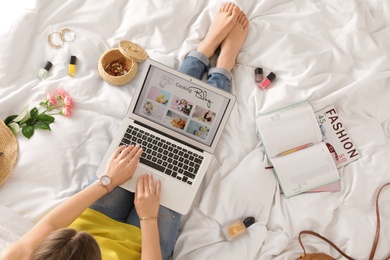 Woman and laptop with open cooking blog on bed, top view