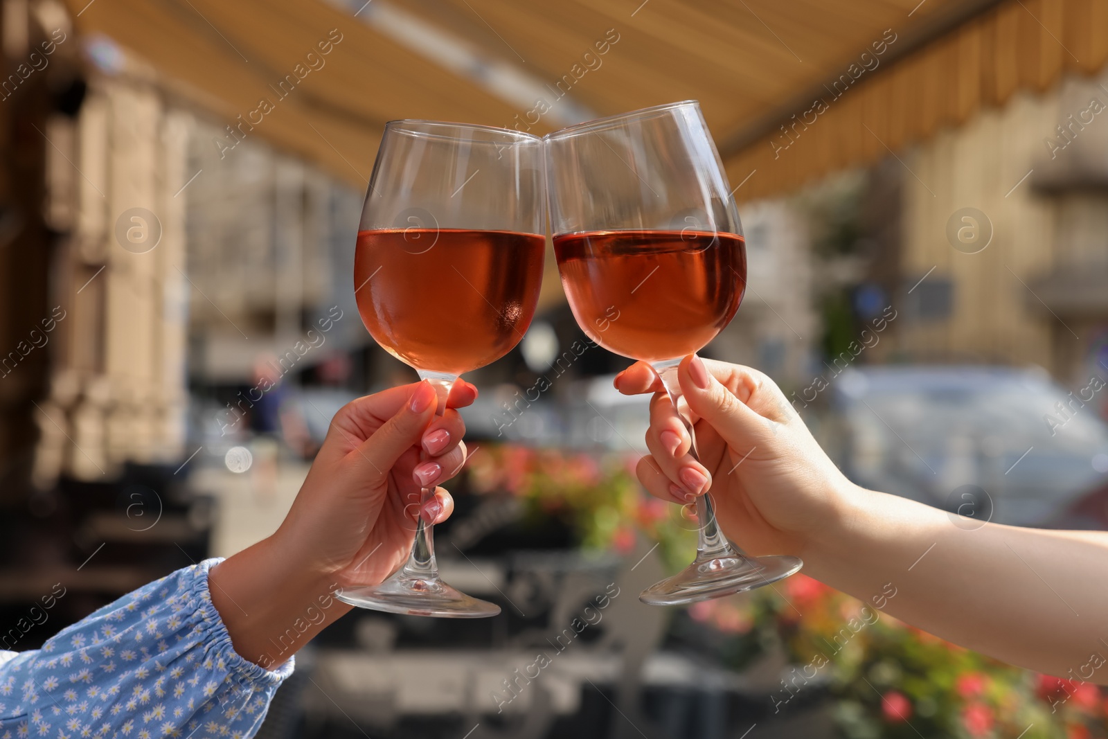 Photo of Women clinking glasses with rose wine in outdoor cafe, closeup