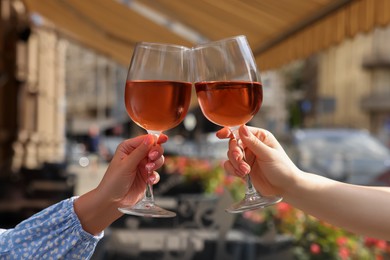 Photo of Women clinking glasses with rose wine in outdoor cafe, closeup