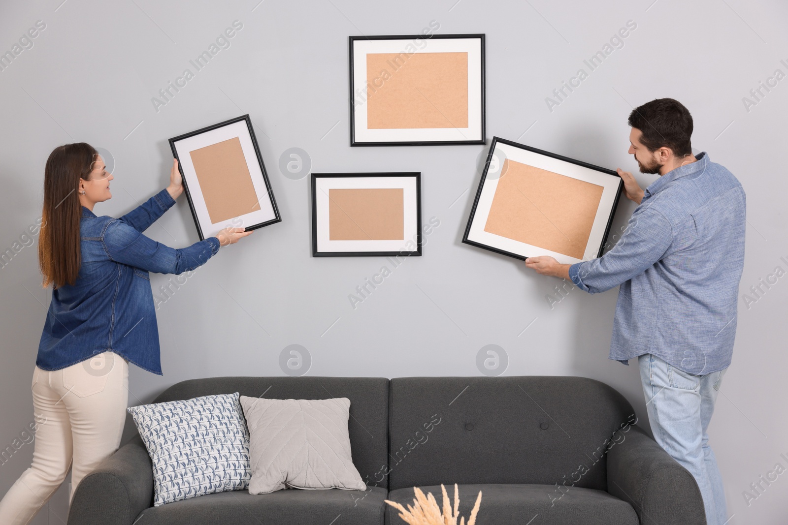 Photo of Man and woman hanging picture frames on gray wall at home