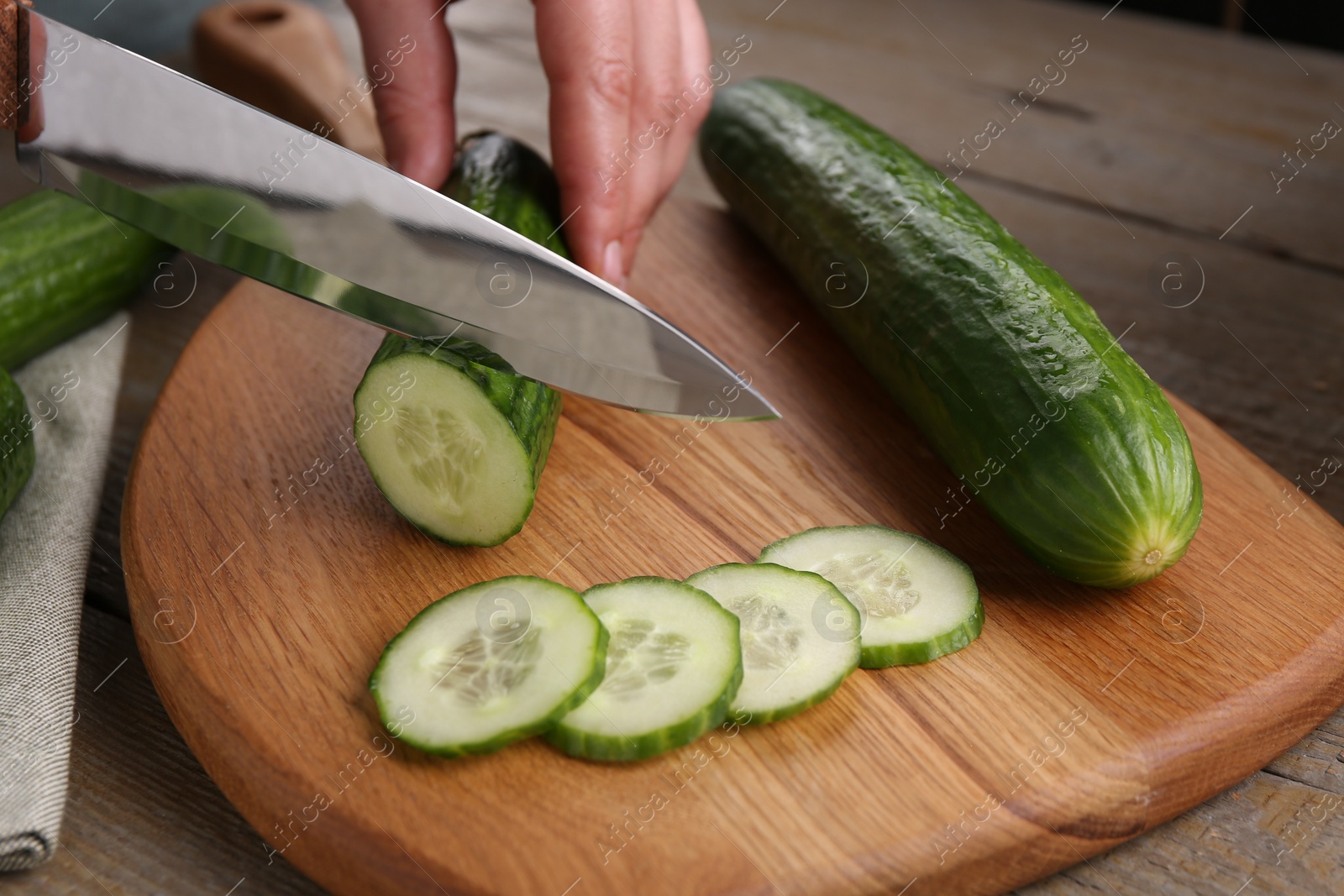 Photo of Woman cutting cucumber on wooden board at table, closeup