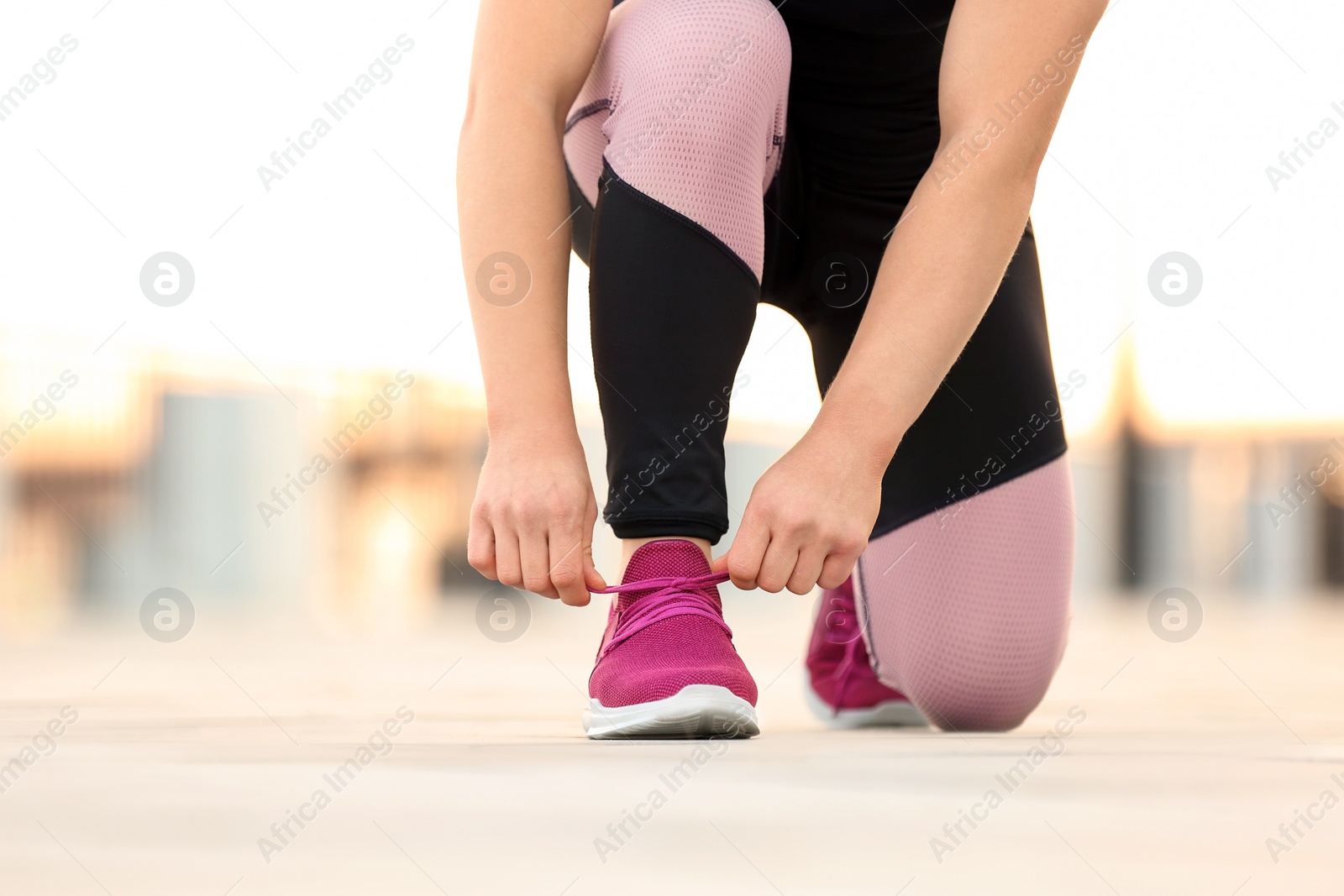 Photo of Young woman tying shoelaces before running outdoors, focus on legs