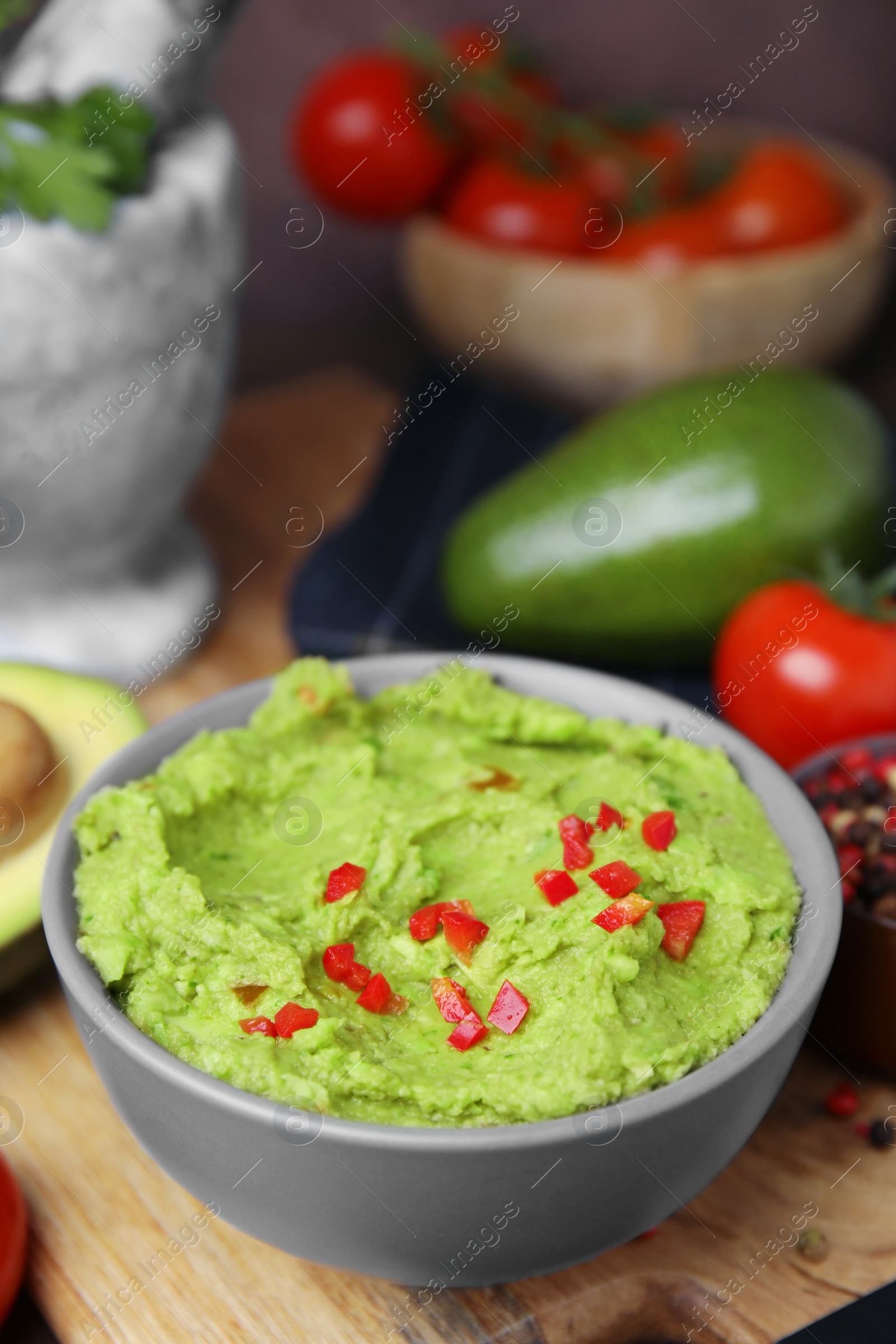 Photo of Bowl of delicious guacamole and ingredients on wooden board, closeup