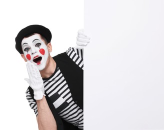 Photo of Funny mime artist peeking out of blank poster on white background