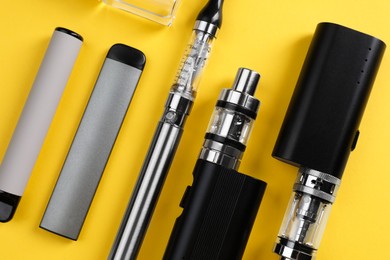 Different electronic cigarettes on yellow background, flat lay