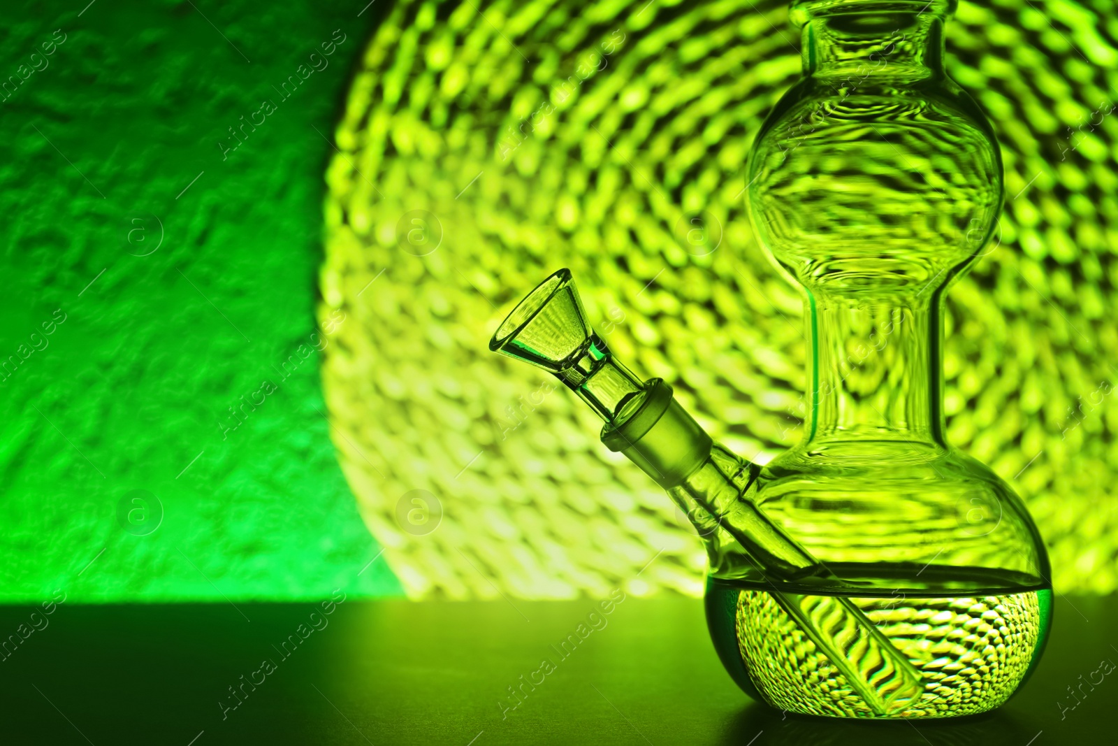 Photo of Closeup view of glass bong on table, space for text. Smoking device