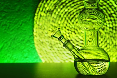 Photo of Closeup view of glass bong on table, space for text. Smoking device