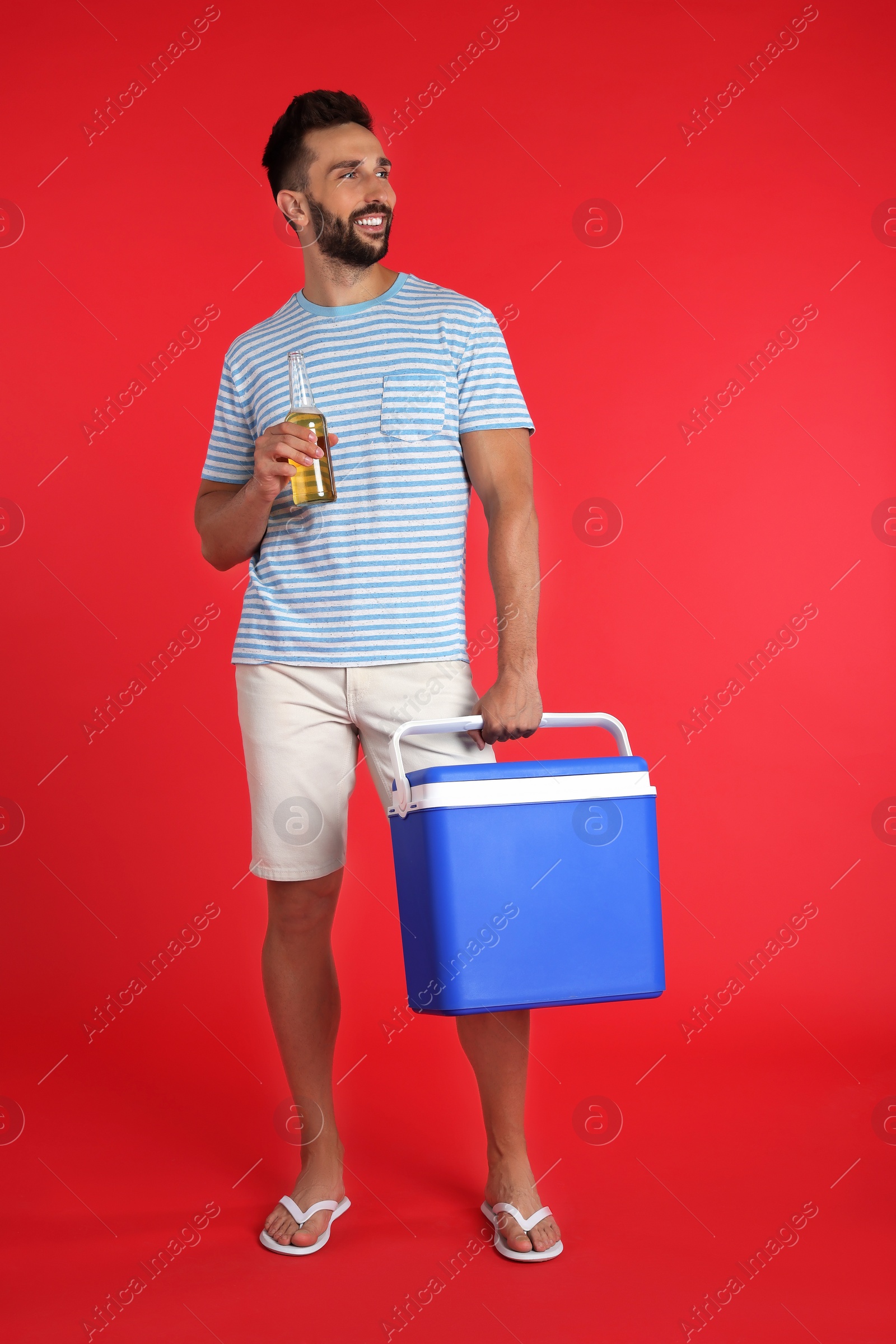 Photo of Happy man with cool box and bottle of beer on red background