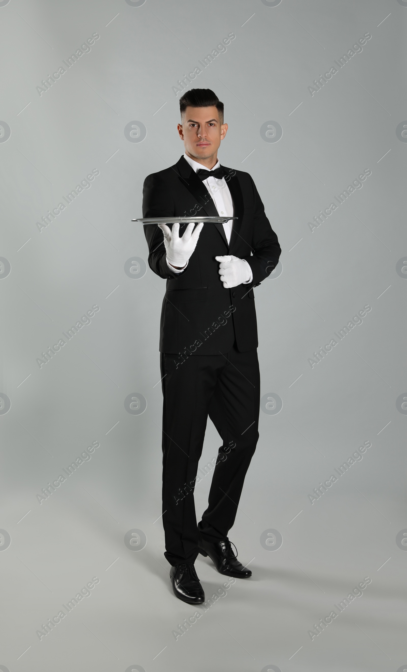 Photo of Handsome butler with tray on light grey background