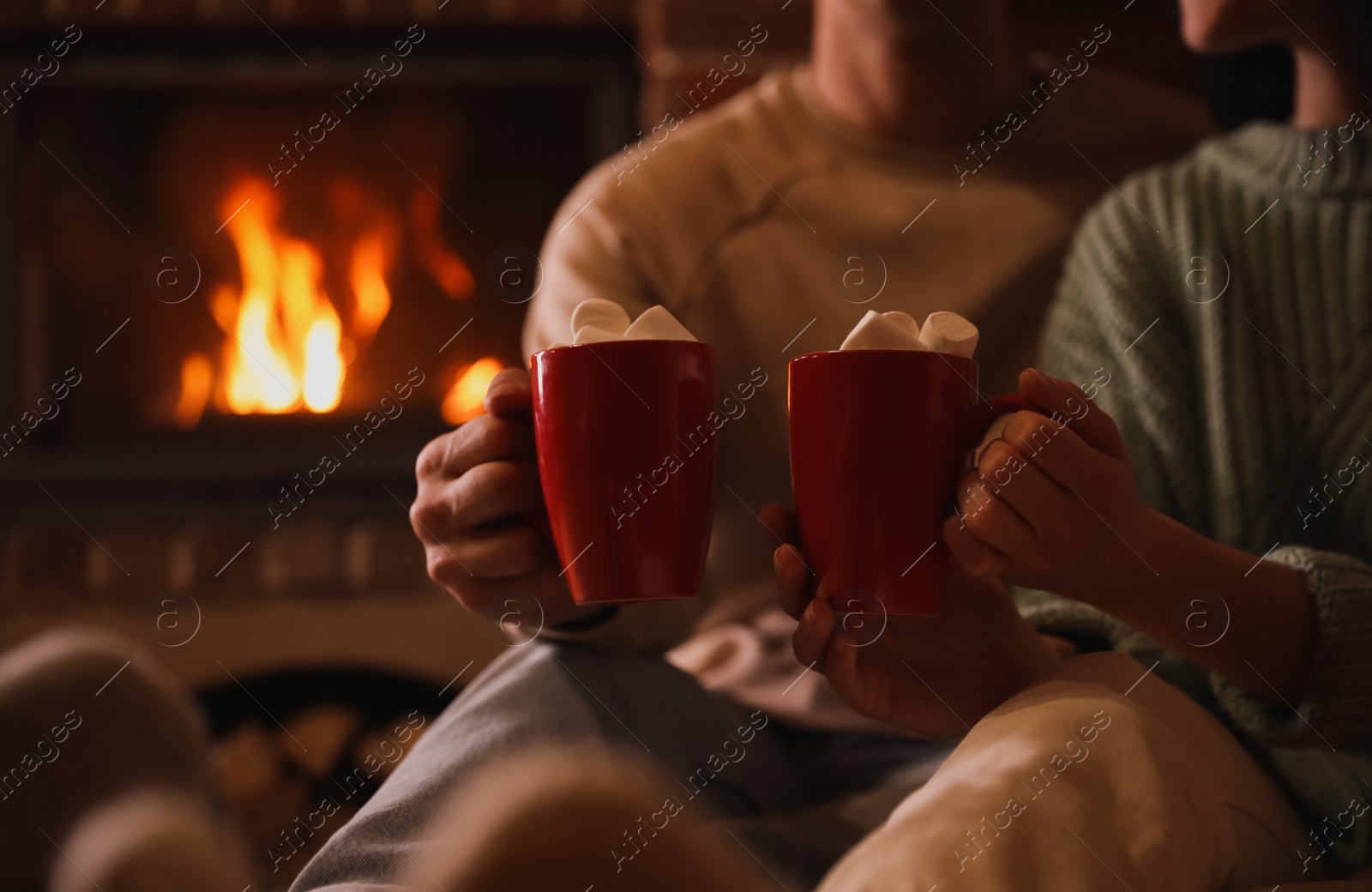 Photo of Lovely couple with sweet cocoa near fireplace indoors, closeup