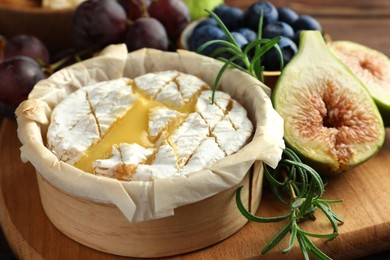 Photo of Tasty baked brie cheese and products on wooden board, closeup