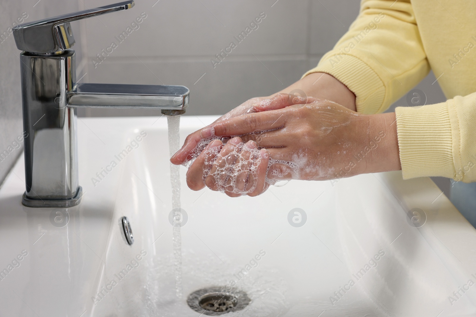 Photo of Woman washing hands with water from tap in bathroom, closeup