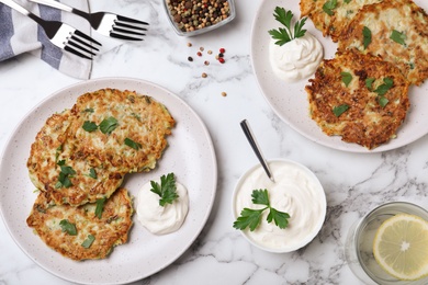 Photo of Delicious zucchini fritters served on white marble table, flat lay