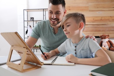 Photo of Boy with father doing homework using tablet at table indoors