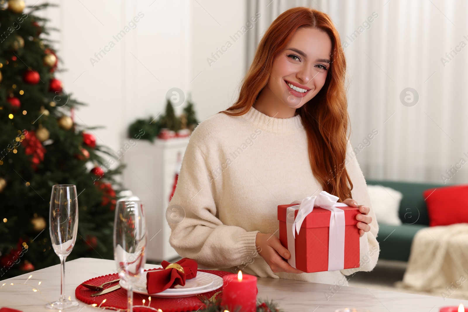 Photo of Beautiful young woman with Christmas gift at served table in room