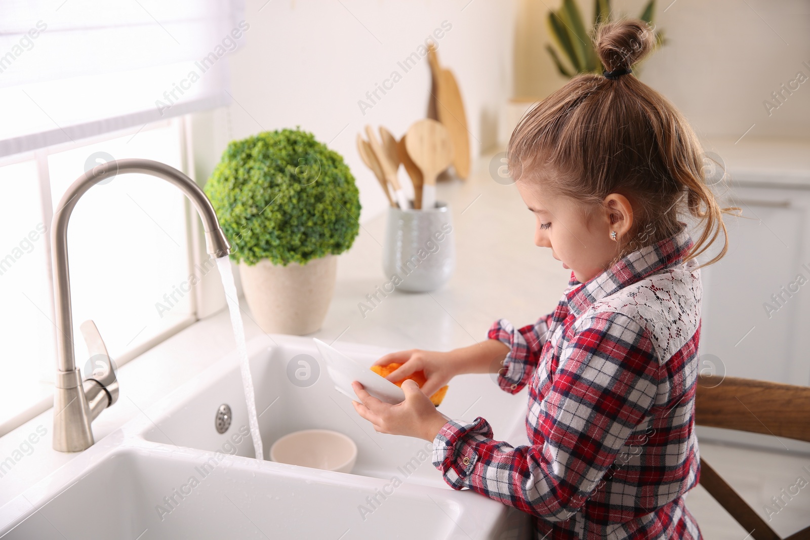 Photo of Little girl washing dishes in kitchen at home