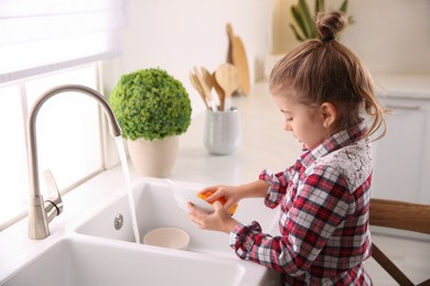 Photo of Little girl washing dishes in kitchen at home