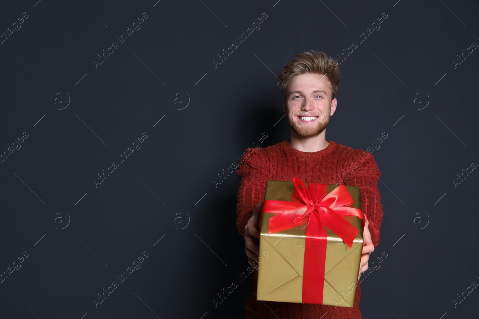 Photo of Young man with Christmas gift on dark background. Space for text