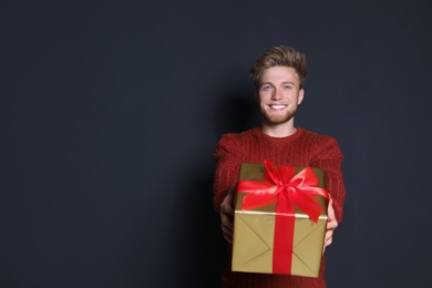 Young man with Christmas gift on dark background. Space for text