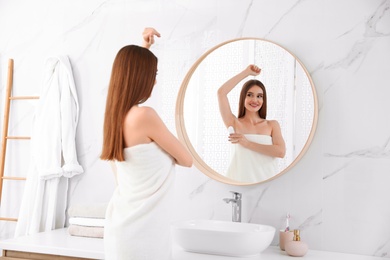 Photo of Beautiful young woman applying deodorant after shower in bathroom