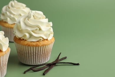 Tasty cupcakes with cream and vanilla pods on green background, closeup. Space for text