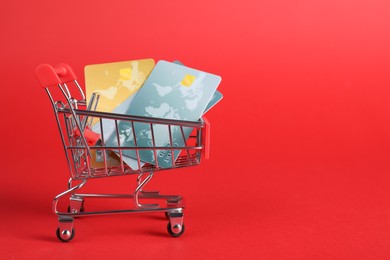 Photo of Small metal shopping cart with credit cards on red background, space for text