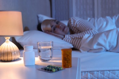 Photo of Mature woman suffering from insomnia in bed at night, focus on nightstand with pills and water