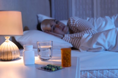 Mature woman suffering from insomnia in bed at night, focus on nightstand with pills and water