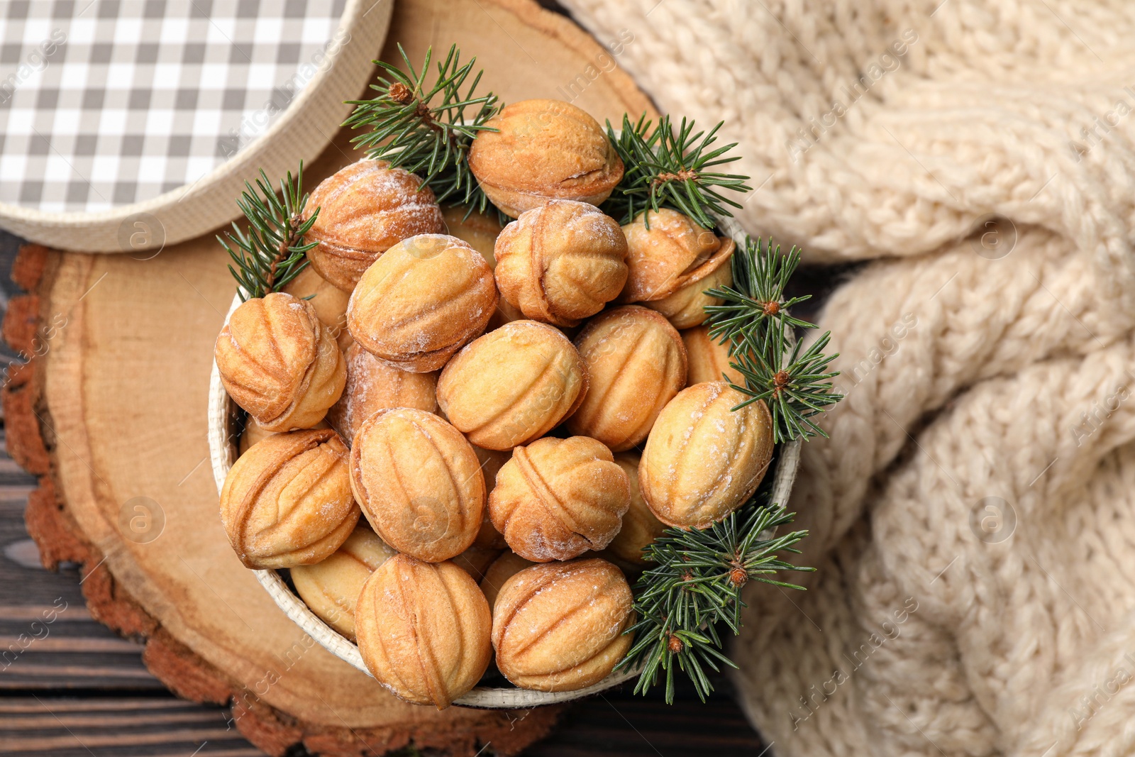 Photo of Bowl of delicious nut shaped cookies and fir tree branches on wooden table, flat lay