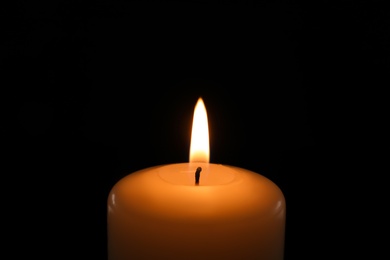 Photo of Wax candle burning on black background, closeup