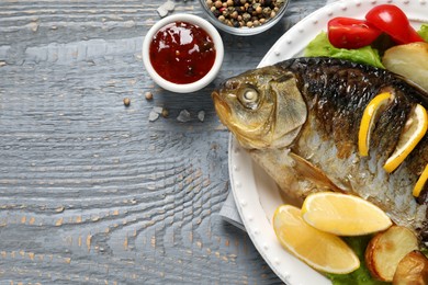 Photo of Tasty homemade roasted crucian carp served on grey wooden table, flat lay and space for text. River fish