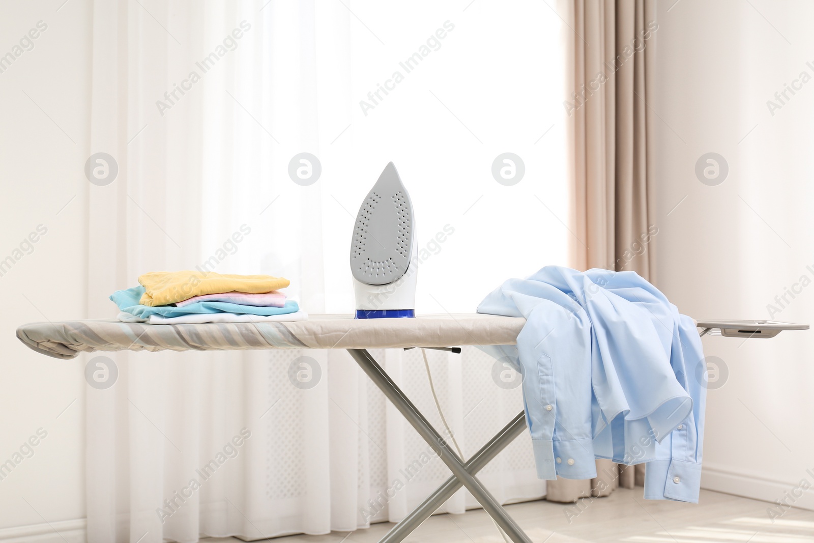 Photo of Board with modern iron and clean clothes indoors. Laundry day