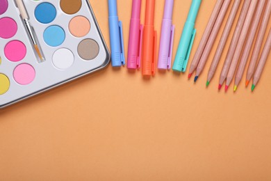 Photo of Watercolor palette, colorful pencils and markers on pale orange background, flat lay. Space for text