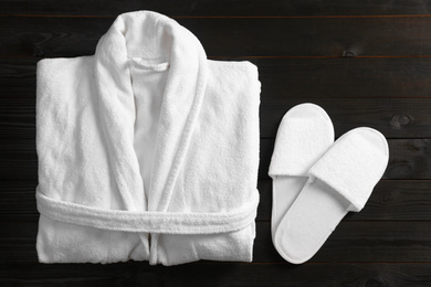 Photo of Clean folded bathrobe and slippers on black wooden background, flat lay