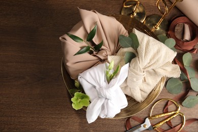 Photo of Furoshiki technique. Flat lay composition with gifts packed in different fabrics and flowers on wooden table